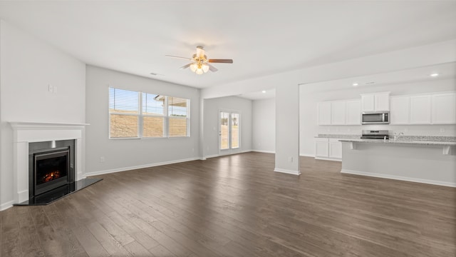 unfurnished living room featuring baseboards, recessed lighting, dark wood-style flooring, ceiling fan, and a lit fireplace