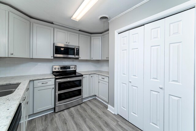 kitchen with appliances with stainless steel finishes, backsplash, light stone counters, light hardwood / wood-style flooring, and gray cabinets