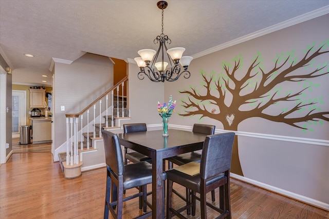 dining space with an inviting chandelier, light wood-type flooring, a textured ceiling, and ornamental molding