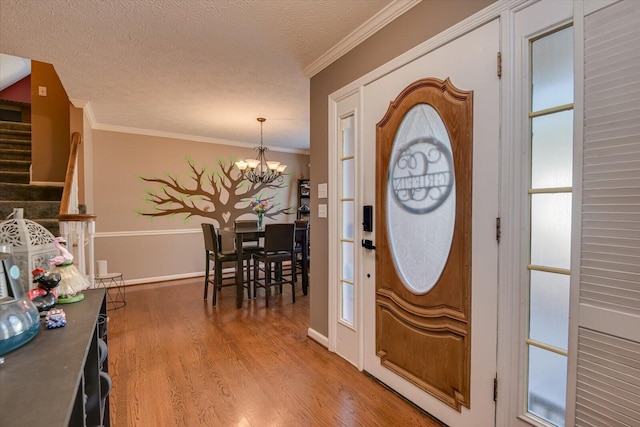 entryway with hardwood / wood-style floors, a textured ceiling, crown molding, and an inviting chandelier