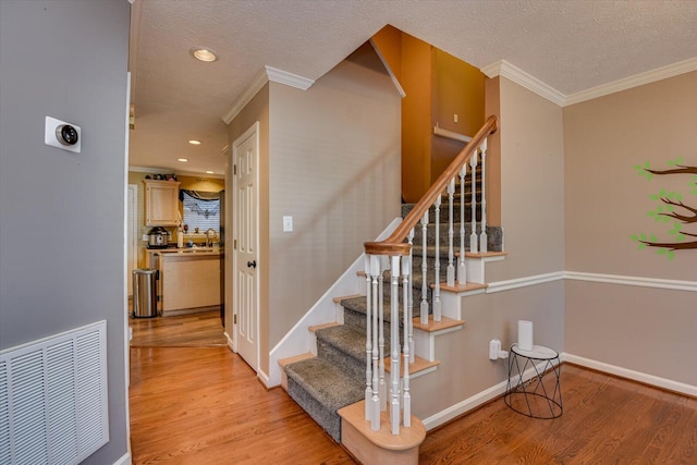 stairs with hardwood / wood-style floors, sink, crown molding, and a textured ceiling