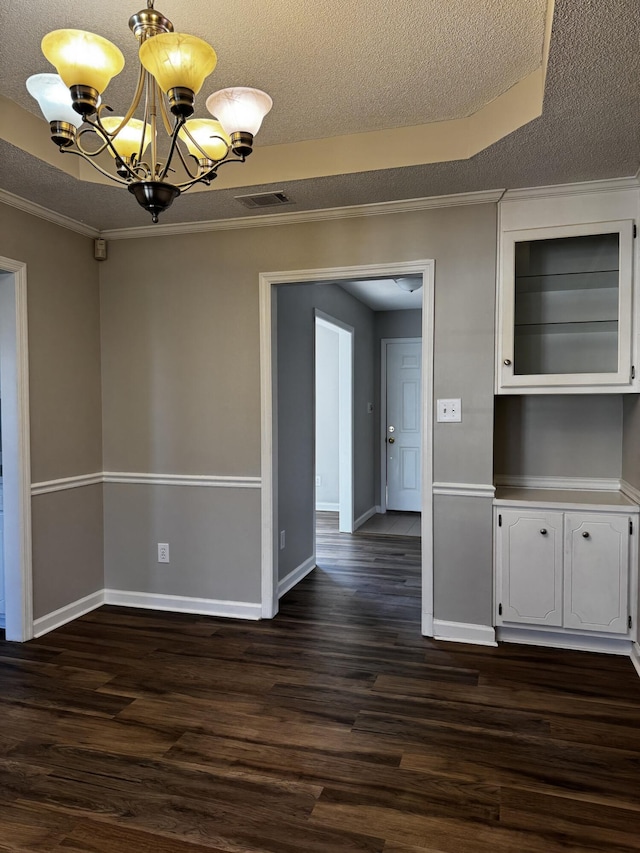 unfurnished dining area featuring a textured ceiling, a chandelier, dark hardwood / wood-style floors, and a raised ceiling