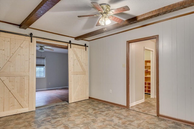 empty room featuring ceiling fan, a barn door, beam ceiling, and wooden walls