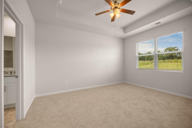 carpeted spare room with a raised ceiling and ceiling fan