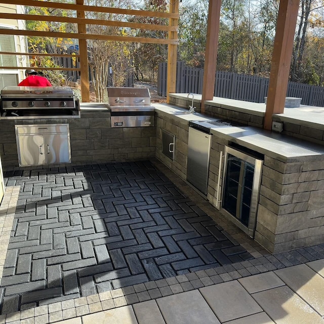 view of patio with grilling area, fence, exterior kitchen, and wine cooler