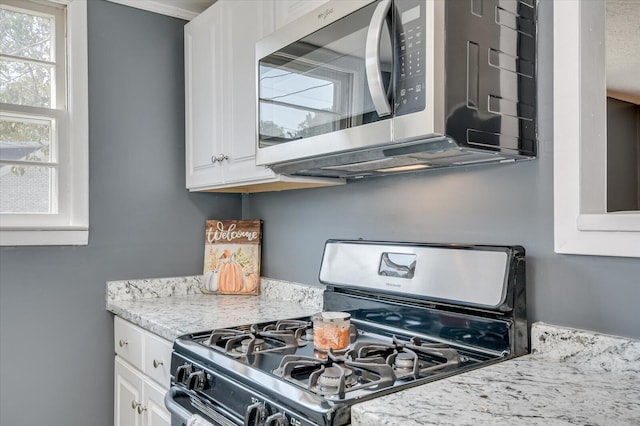 kitchen featuring white cabinets, black gas stove, and light stone countertops