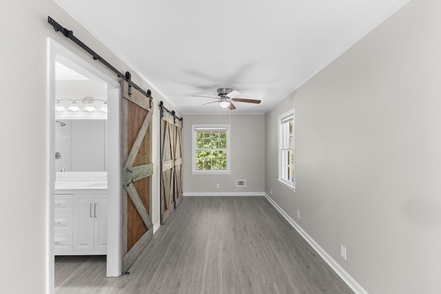 interior space with a barn door, hardwood / wood-style flooring, ceiling fan, and crown molding