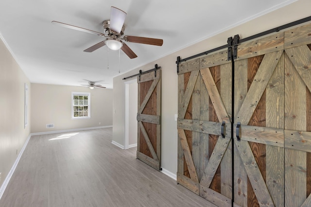 empty room with ceiling fan, a barn door, ornamental molding, and light hardwood / wood-style flooring