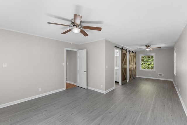 spare room with a barn door, crown molding, hardwood / wood-style floors, and ceiling fan