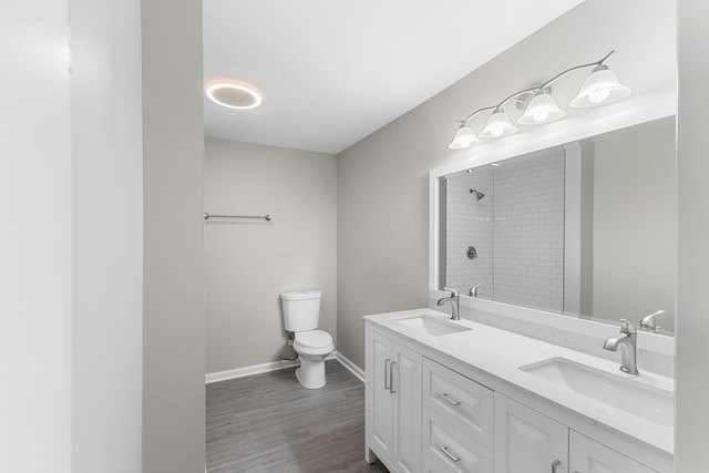 bathroom featuring a tile shower, hardwood / wood-style floors, vanity, and toilet