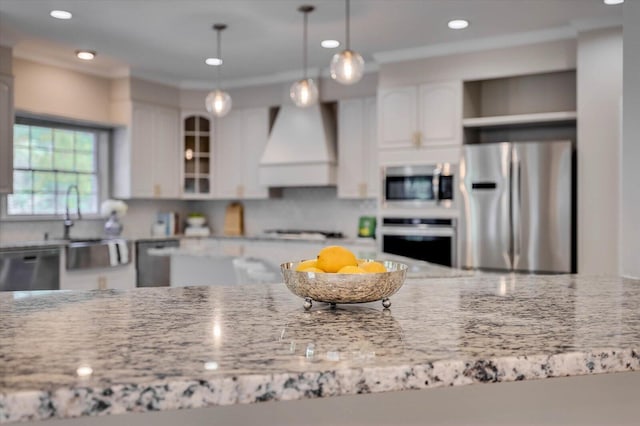 kitchen with pendant lighting, white cabinets, light stone countertops, custom range hood, and stainless steel appliances