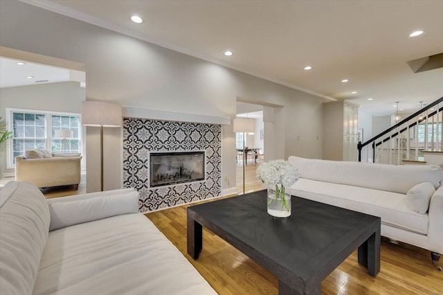 living room with a fireplace, light wood-type flooring, crown molding, and lofted ceiling