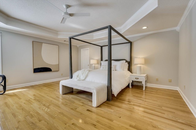 bedroom with crown molding, hardwood / wood-style flooring, ceiling fan, a textured ceiling, and a tray ceiling