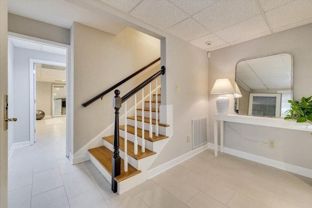 stairs featuring a paneled ceiling and tile patterned flooring