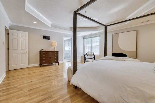 bedroom with a textured ceiling, light wood-type flooring, a raised ceiling, and ornamental molding