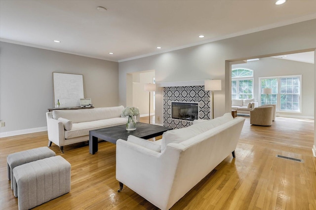 living room with a tile fireplace, crown molding, light hardwood / wood-style flooring, and vaulted ceiling