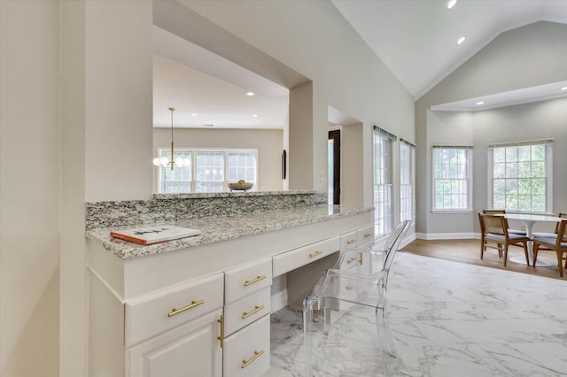 kitchen featuring light stone countertops, pendant lighting, lofted ceiling, white cabinets, and built in desk