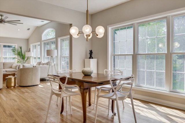 dining room with vaulted ceiling, ceiling fan with notable chandelier, and light wood-type flooring