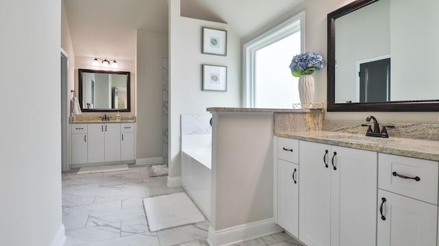 full bath with baseboards, two vanities, marble finish floor, and a garden tub