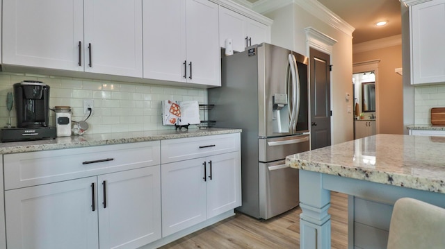 kitchen featuring crown molding, light stone countertops, light wood-style floors, stainless steel fridge, and white cabinets