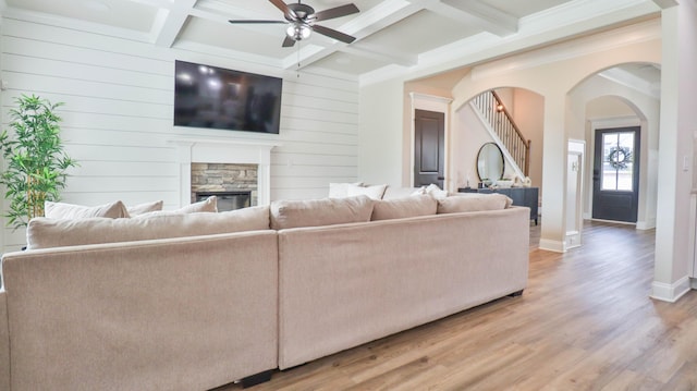 living area featuring wood finished floors, beam ceiling, a fireplace, arched walkways, and a ceiling fan