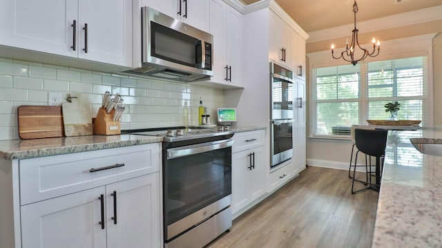kitchen featuring appliances with stainless steel finishes, tasteful backsplash, a notable chandelier, light wood-style floors, and white cabinetry