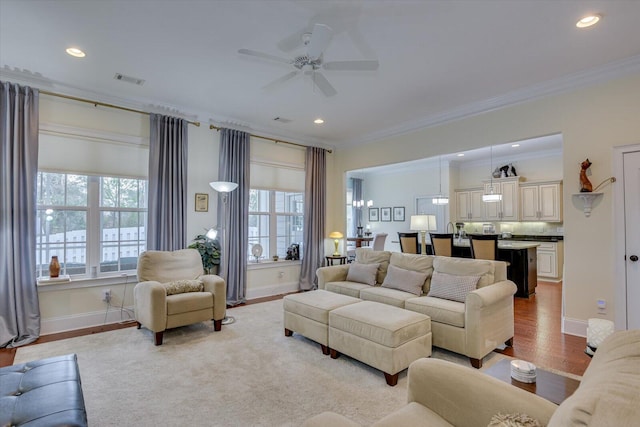 living room with visible vents, light wood-style flooring, ornamental molding, baseboards, and ceiling fan