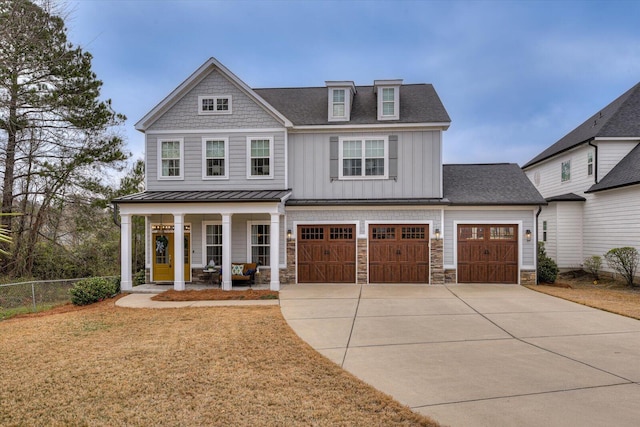 view of front of house with board and batten siding, fence, concrete driveway, covered porch, and stone siding