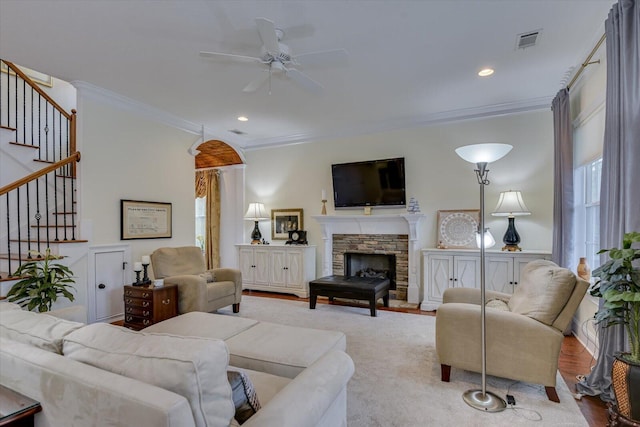 living room featuring stairway, visible vents, a fireplace, ornamental molding, and ceiling fan