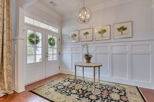 entrance foyer featuring visible vents, wood finished floors, crown molding, a decorative wall, and a chandelier