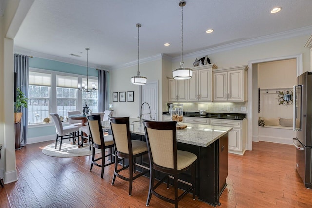 kitchen with crown molding, an island with sink, decorative backsplash, freestanding refrigerator, and light wood-style floors