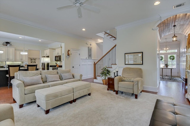 living area with visible vents, crown molding, light wood-type flooring, and stairs