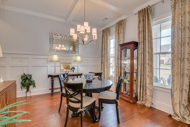 dining area with beamed ceiling, a decorative wall, an inviting chandelier, and hardwood / wood-style floors