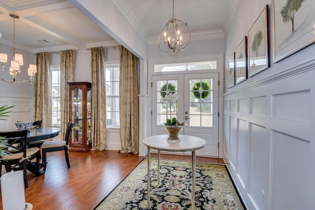 foyer entrance with hardwood / wood-style floors, an inviting chandelier, a decorative wall, and ornamental molding