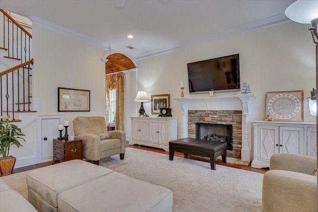 living area featuring visible vents, crown molding, stairs, a stone fireplace, and wood finished floors