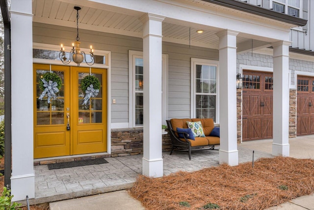 doorway to property with a porch, french doors, a garage, and stone siding