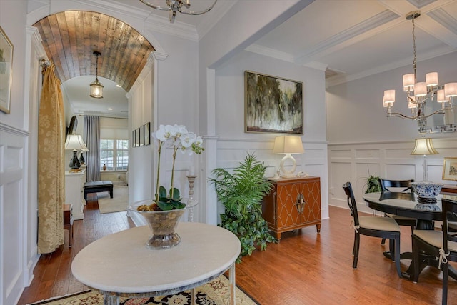 dining area with coffered ceiling, wood-type flooring, crown molding, a decorative wall, and a chandelier