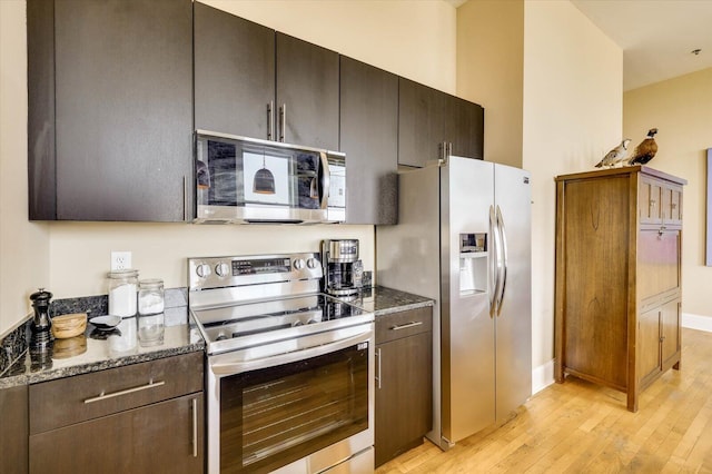 kitchen featuring dark stone countertops, light hardwood / wood-style flooring, dark brown cabinets, and appliances with stainless steel finishes