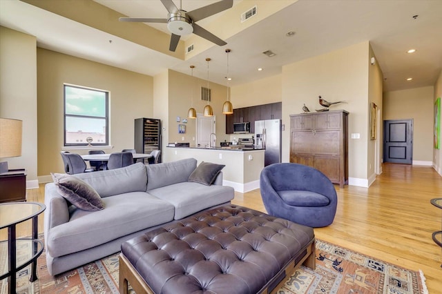 living room featuring ceiling fan, sink, a towering ceiling, and light wood-type flooring