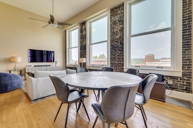 dining room with ceiling fan, light wood-type flooring, brick wall, and vaulted ceiling