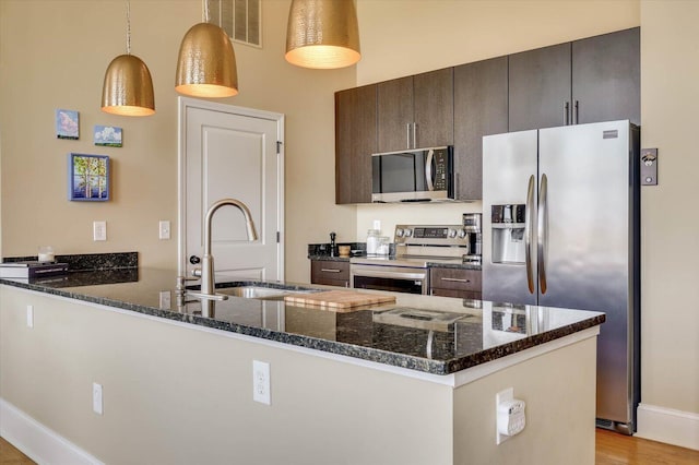 kitchen with dark stone counters, hanging light fixtures, sink, appliances with stainless steel finishes, and dark brown cabinets