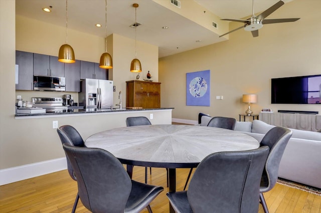 dining room featuring ceiling fan, light hardwood / wood-style floors, a towering ceiling, and sink