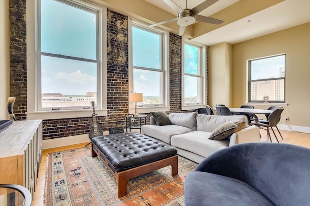 living room featuring ceiling fan, a healthy amount of sunlight, brick wall, and light hardwood / wood-style flooring