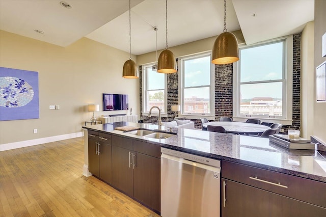 kitchen with stainless steel dishwasher, dark brown cabinetry, sink, dark stone countertops, and hanging light fixtures