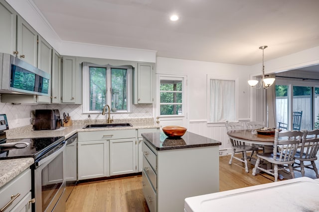 kitchen with appliances with stainless steel finishes, a sink, light wood-type flooring, a center island, and wainscoting