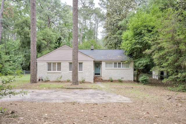 ranch-style home with fence, a chimney, brick siding, a shingled roof, and view of wooded area