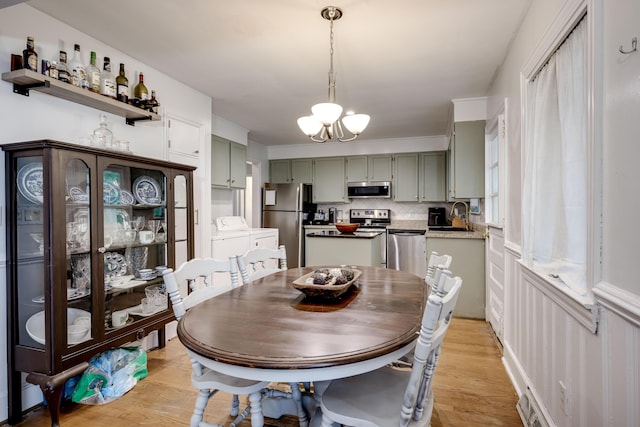 dining area with independent washer and dryer, light wood-type flooring, and a chandelier