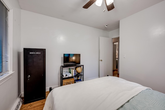bedroom with a baseboard radiator, light wood-type flooring, ceiling fan, and baseboards