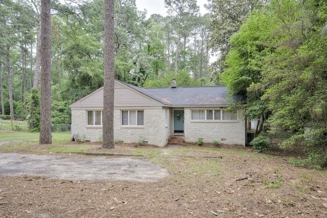 ranch-style home featuring crawl space, brick siding, fence, roof with shingles, and view of scattered trees