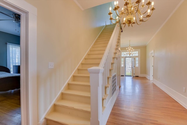 staircase with hardwood / wood-style flooring, ceiling fan with notable chandelier, and crown molding